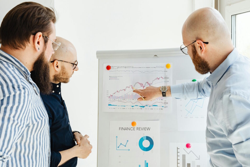 Three business professionals analyzing financial charts and graphs on a whiteboard, discussing trends and insights related to gambling behavior and market performance