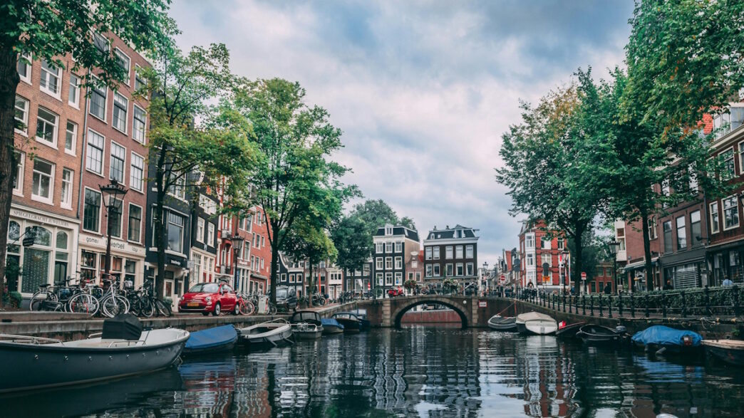 A scenic canal in the Netherlands, lined with traditional Dutch buildings and boats, reflecting the urban charm of Amsterdam